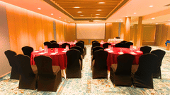 A well-lit conference room at Pride Plaza Ahmedabad, featuring round tables with red tablecloths, arranged in a U-shape for a meeting or presentation.